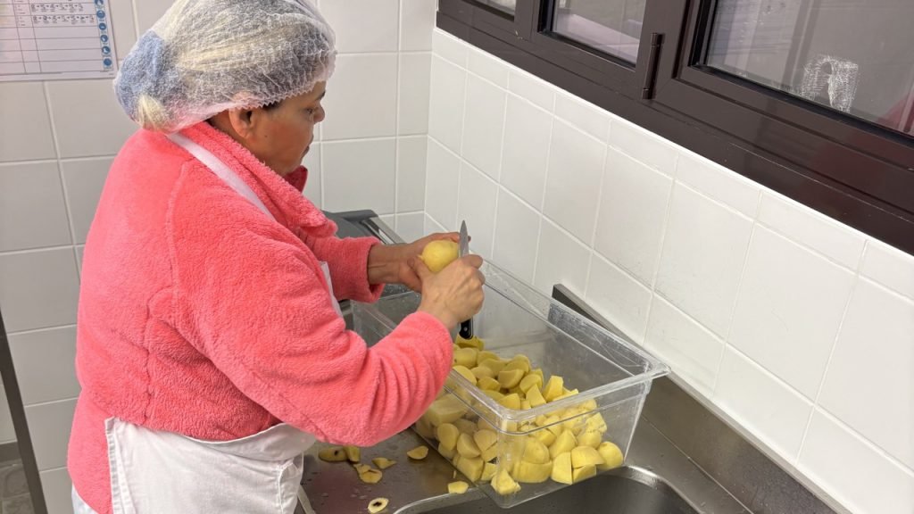 Kitchen staff member peeling fresh potatoes by hand in a French school kitchen.