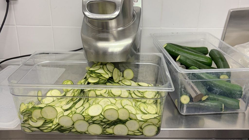 Large batch of sliced zucchini prepared in a French school kitchen for lunch service.