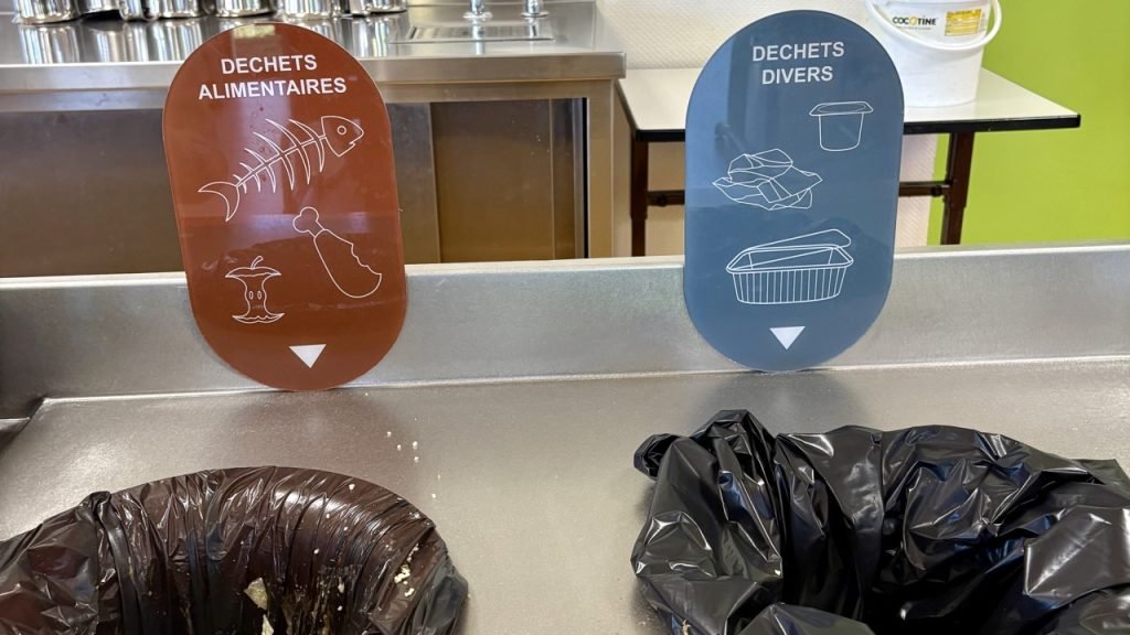 Food waste sorting station in a French school cafeteria showing bins for food scraps and mixed waste.
