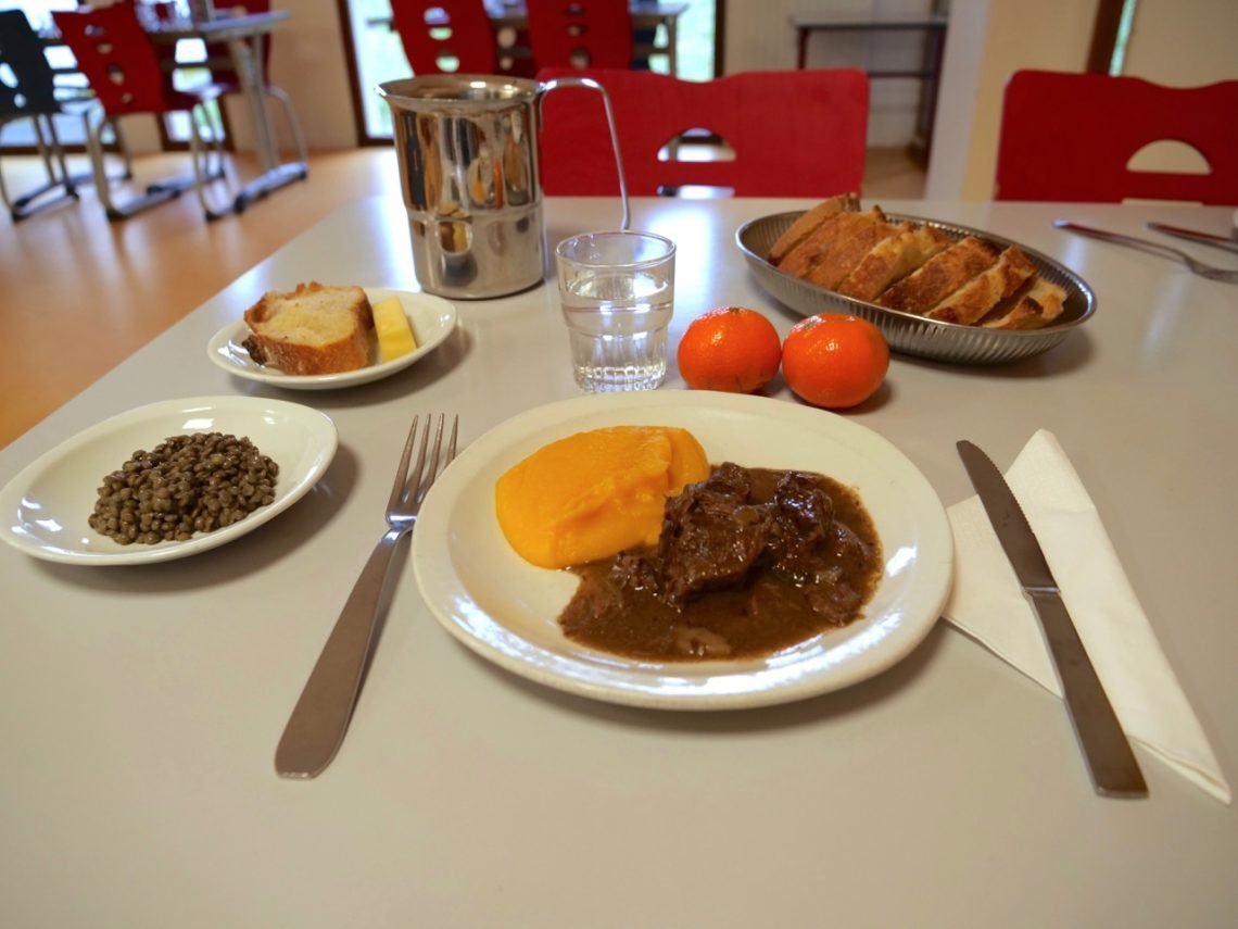 Healthy French school lunch tray with vegetables, main dish, fruit, bread, water pitcher, glass of water.